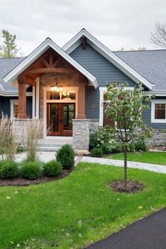 a blue house with stone and wood trimming on the front door, windows, and landscaping