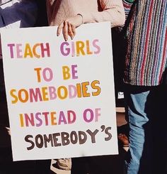 a woman holding a sign that says teach girls to be somebody instead of somebody's