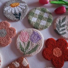 six crocheted flower coasters on a table with tulips in the background