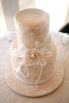 a three tiered wedding cake with white lace and flowers on the top, sitting on a table