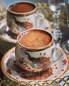 two cups filled with hot chocolate sitting on top of saucers and plates next to each other