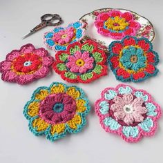 several crocheted flowers are arranged on a white surface with scissors and other items