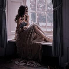 a woman sitting on a window sill reading a book