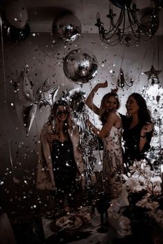 three women standing in front of balloons and confetti