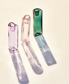 three different colored glass bottles sitting on top of a white table next to each other