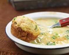 a white bowl filled with soup and a muffin on top of a wooden table