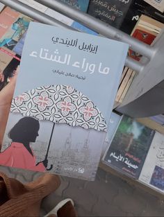 a person holding up a book in front of bookshelves with arabic writing on them