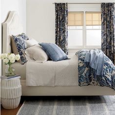 a bed with blue and white pillows in a bedroom next to a window covered by curtains