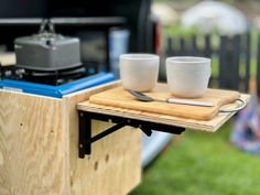 two cups are sitting on top of a cutting board with a knife and fork next to it