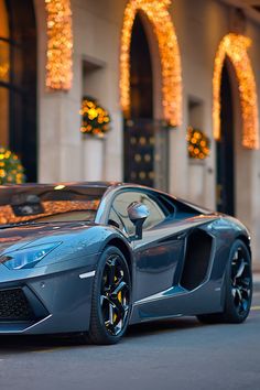 a blue sports car parked in front of a building with christmas lights on the windows