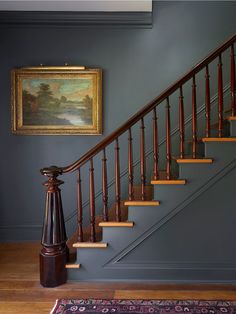 a painting hangs on the wall next to a stair case in a blue painted room