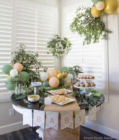 a baby shower party with balloons, greenery and desserts on a round table