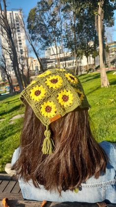 a woman sitting on top of a wooden bench wearing a hat with sunflowers