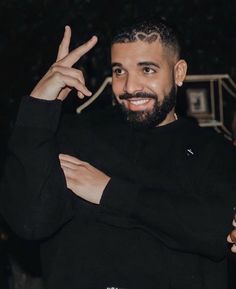 a man with a goatee smiles and holds his hand up in the air while wearing a black sweater