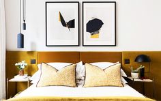 two framed pictures hang above a bed with yellow linens and pillows on the headboard