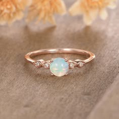 a white opal and diamond ring sitting on top of a table next to flowers