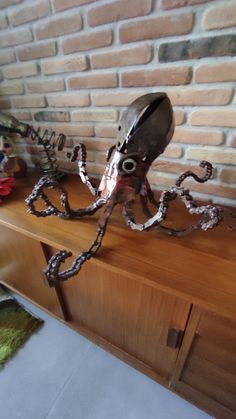 an octopus sculpture sitting on top of a wooden table next to a brick wall with chains hanging from it's sides