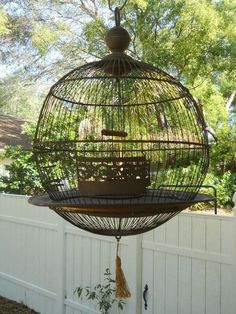 a bird cage hanging from the side of a white fence