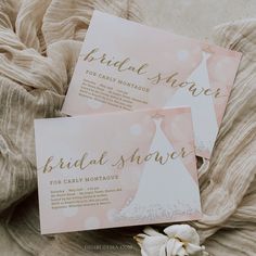 two pink and gold bridal shower cards on top of a bed with white flowers