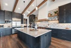 a large kitchen with wooden floors and black cabinets, white counter tops and wood beams