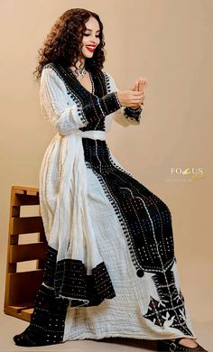 a woman in a white and black dress is sitting on a chair with her hands together