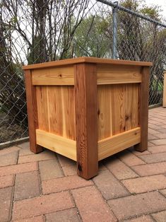 a wooden planter sitting on top of a brick floor next to a fence and trees