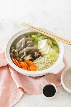 a white bowl filled with vegetables and chopsticks on top of a pink napkin