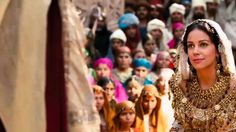 a woman in a gold dress and headdress standing next to a group of people