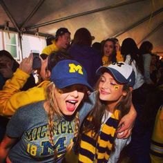 two girls with their arms around each other in front of a crowd at a football game