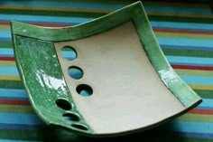 a green and white plate with holes in the center on a striped tableclothed surface