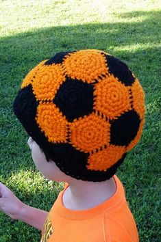 a young boy wearing an orange and black knitted soccer ball hat