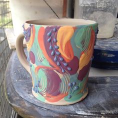 a colorful coffee cup sitting on top of a table next to a potted plant