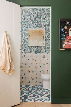 a bathroom with green walls and colorful tile on the wall, along with a white toilet