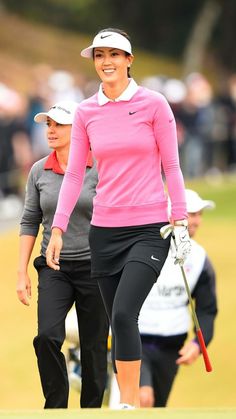 a woman in pink shirt and black pants walking on the golf course with her caddy