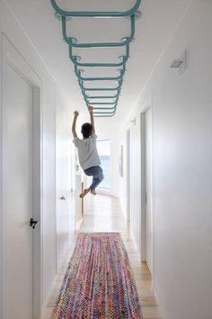 a person jumping up into the air on a rug in a hallway with white walls and wooden floors