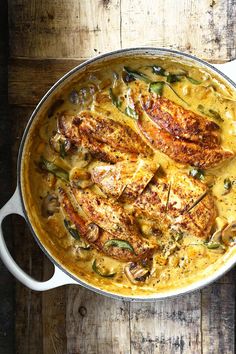 a pan filled with chicken and vegetables on top of a wooden table