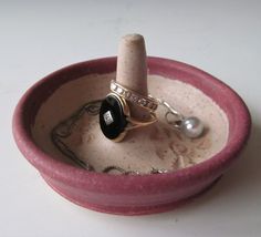 a pink bowl with a ring in it and a pearl on the side, sitting on a table