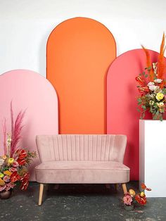 a pink couch sitting in front of an orange and pink wall with flowers on it