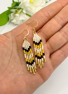 a pair of yellow and black beaded earrings sitting on top of a person's hand