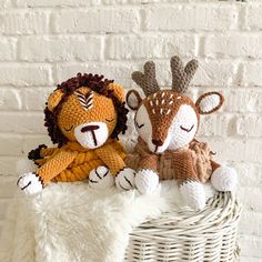 two stuffed animals sitting in a basket on top of a white blanket next to a brick wall