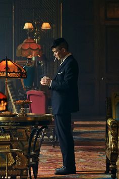 a man in a suit standing next to a table with a lamp on top of it