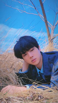 a boy laying in the grass with his hand on his head and looking at the camera