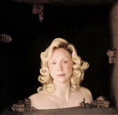 a painting of a woman with blonde hair in a black box looking at the camera