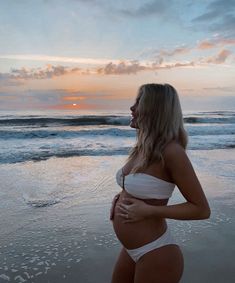 a pregnant woman standing on the beach at sunset