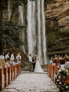 a bride and groom are standing in front of a waterfall at their wedding ceremony, surrounded by wooden pews