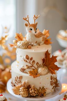 a three tiered white cake decorated with gold leaves and deer figurines