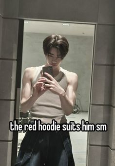 a man looking at his cell phone while standing in front of a mirror with the caption, the red hoodie suits him sm