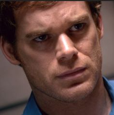 a close up of a person wearing a blue shirt and looking at the camera with a serious look on his face