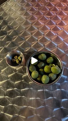 a bowl filled with green olives on top of a metal table