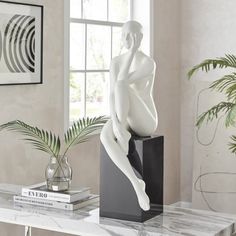 a white statue sitting on top of a table next to a plant and vases